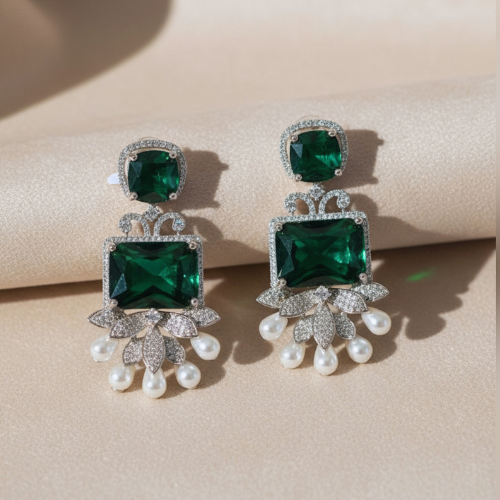 Drop earrings with two green glass stones, American diamond petals, and pearl drops, displayed on a nude satin background