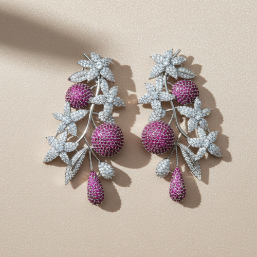Diamond-shaped silver drop earrings with purple gemstones and crystal detailing, displayed on a smooth beige satin background.