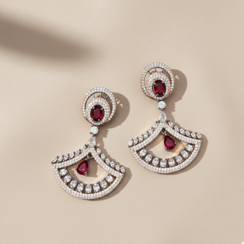 Fan-shaped drop earrings with sparkling diamonds and red rubies in an openwork design, displayed on a soft beige textured background.